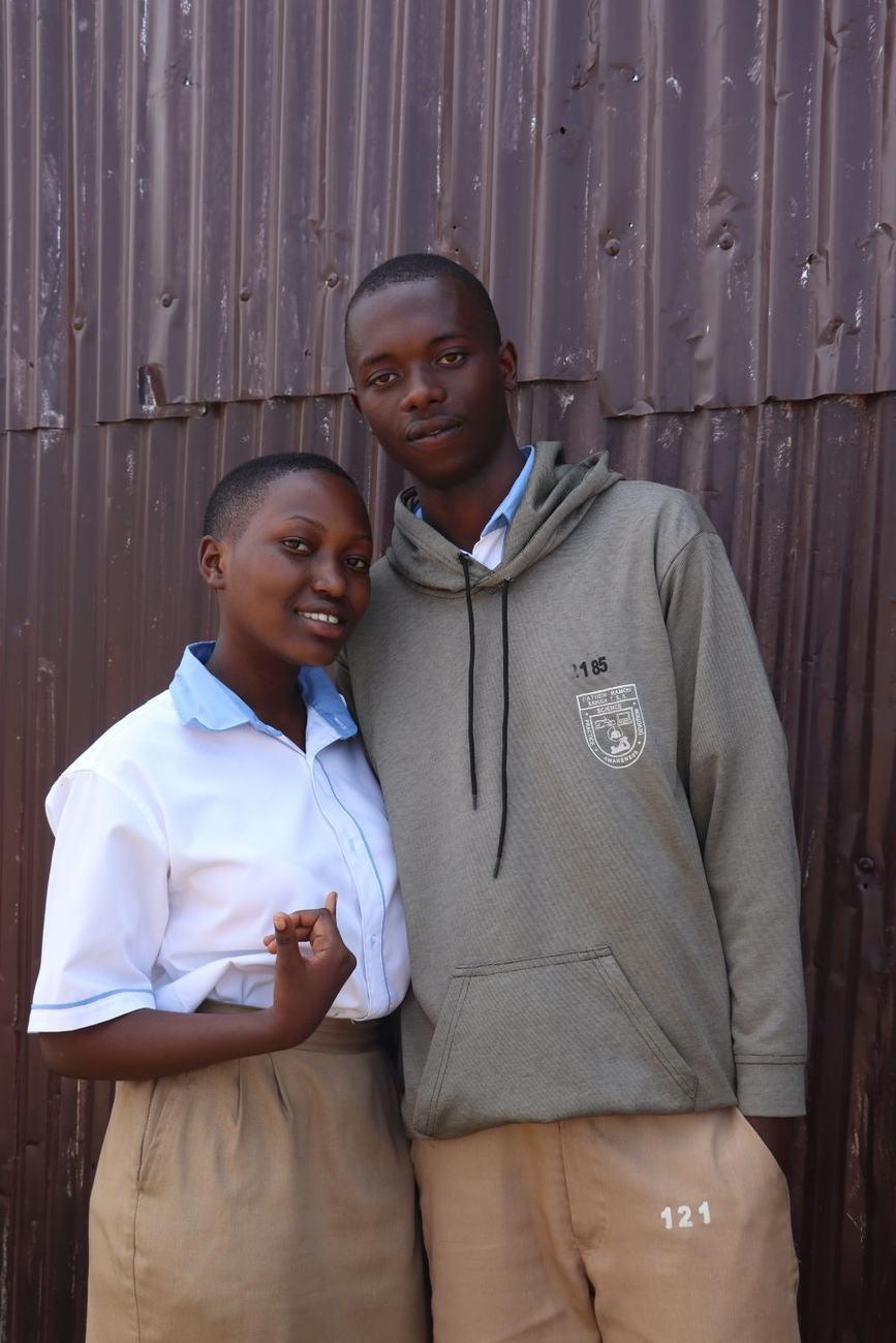 Two teenagers standing together against a corrugated wall