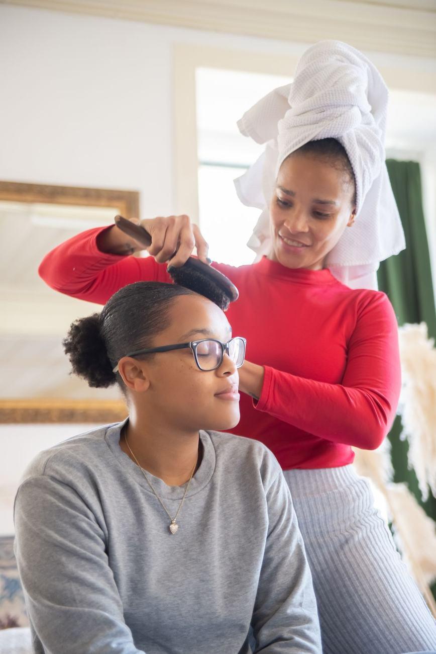 A mother lovingly brushing her teenage daughter’s hair