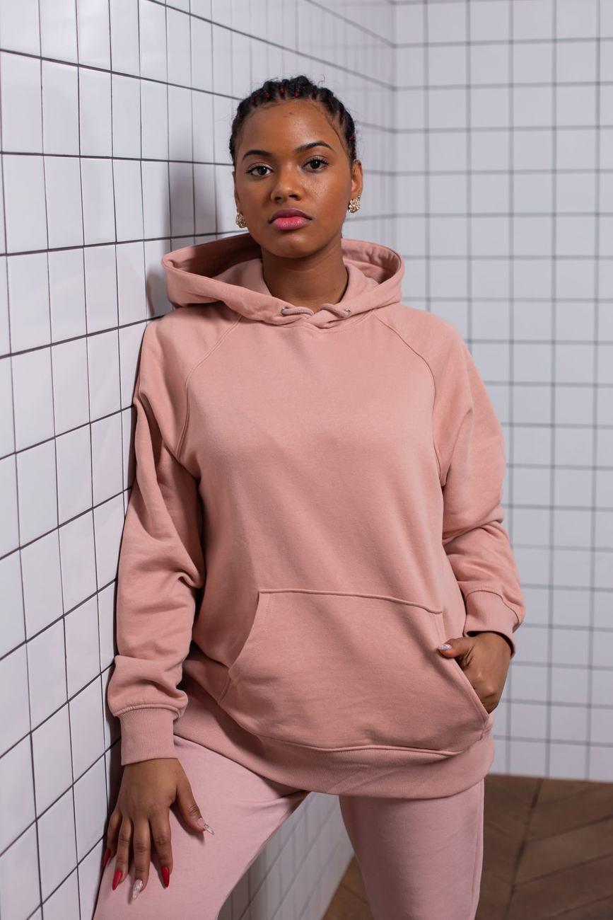 A young woman in a pink hoodie standing against a tiled wall
