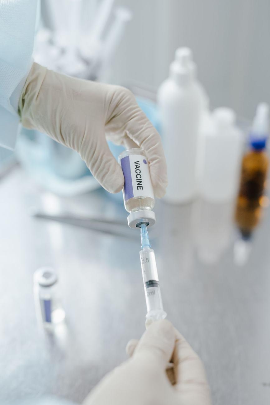 A health worker in gloves preparing a vaccine syringe