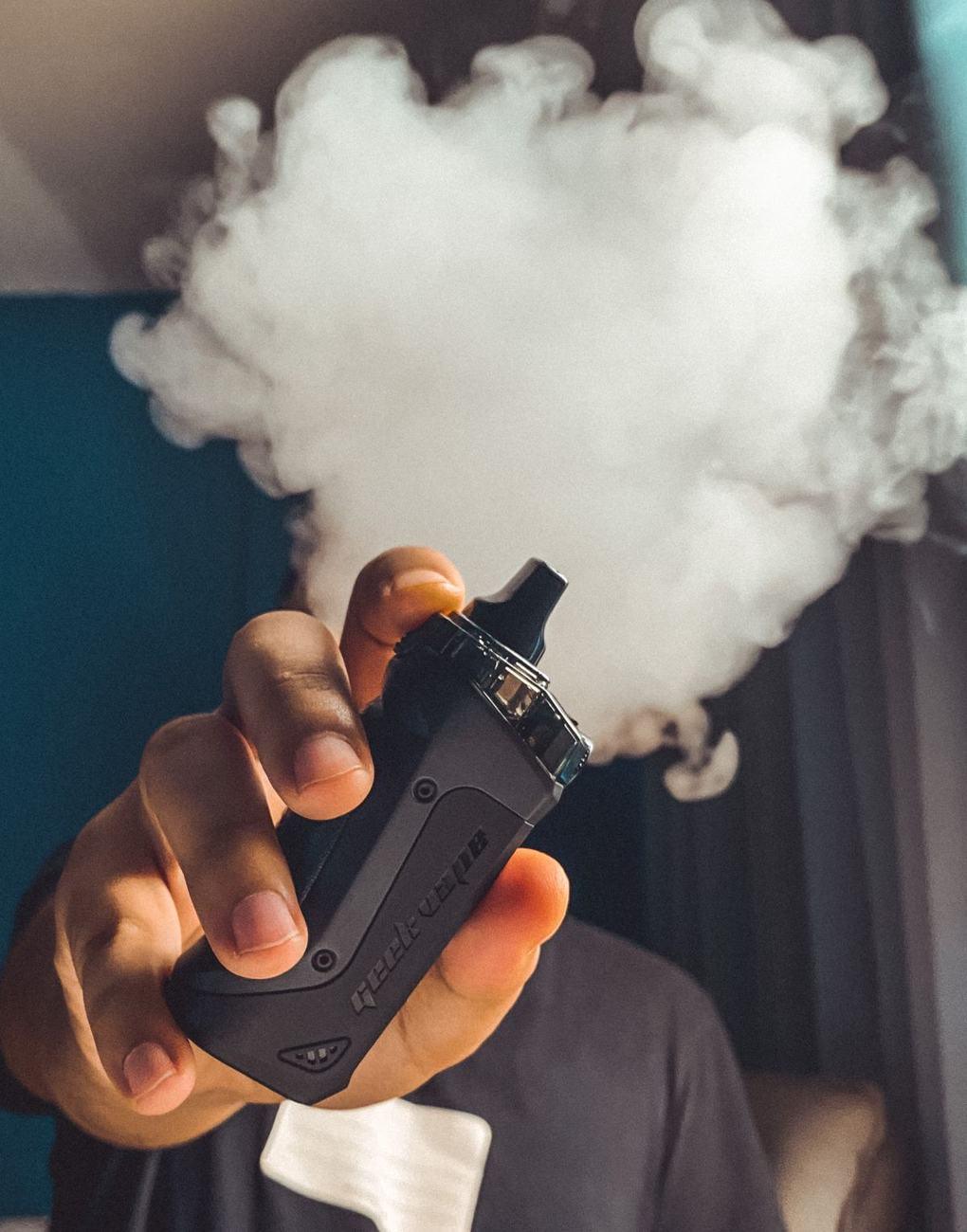 A hand holding a vape device releasing a cloud of vapour
